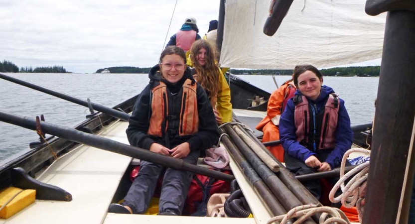 A group of students wearing life jackets hold the oars of a sailboat 